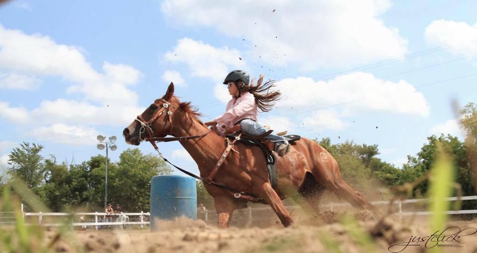A rider and chestnut horse leaping over a barrel at a competition