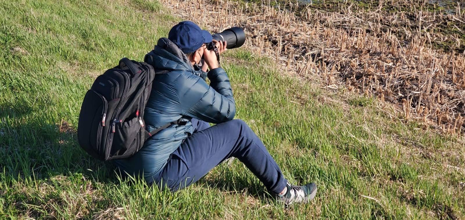 Ramakanth Kandlakunta crouches at a field edge with his camera and telephoto lens